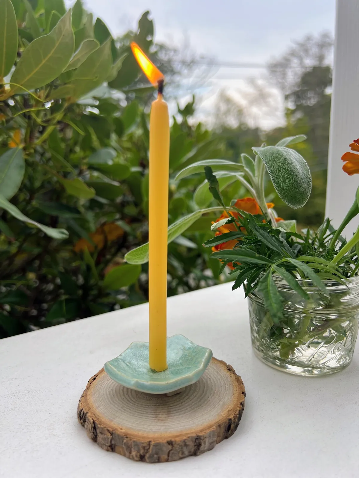 A lit beeswax taper in a sage-green ceramic holder